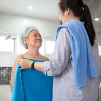 An elderly woman taking a bath and being assisted by a female