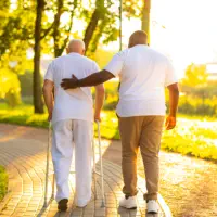 A male assisting the elderly man to walk outside