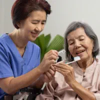 A female caregiver helping an elderly woman to brush her teeth