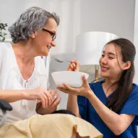 A female caregiver feeding an elderly woman