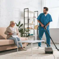 A male caregiver cleaning the room of an elderly woman