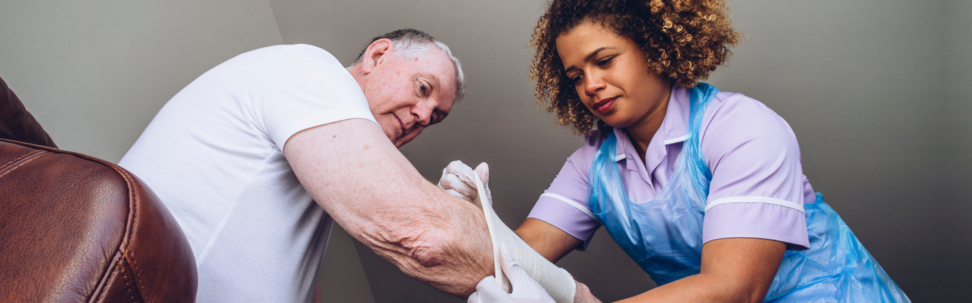 A female caregiver helping an elderly man to put clothes
