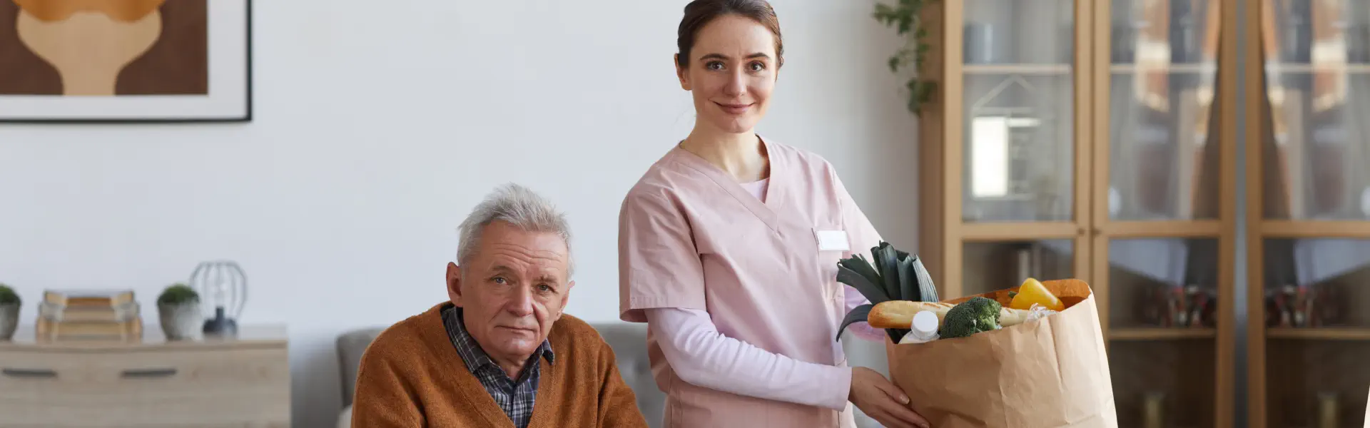 An elderly man sitting on a wheelchair and a female caregiver preparing a meal
