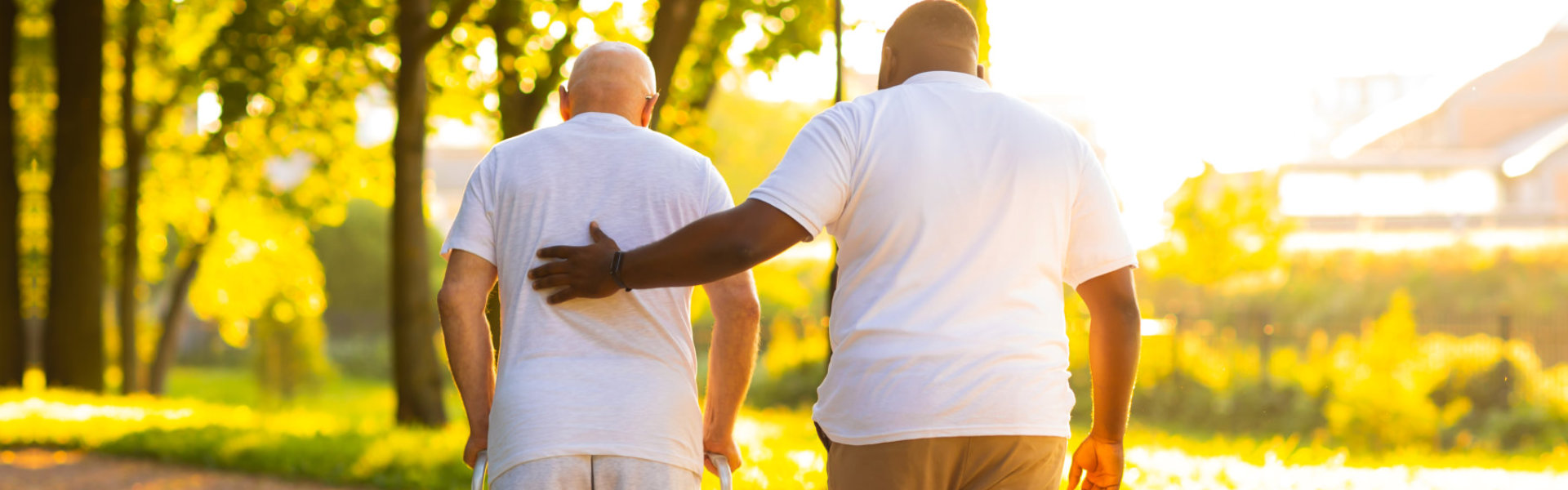 A male assisting the elderly man to walk outside