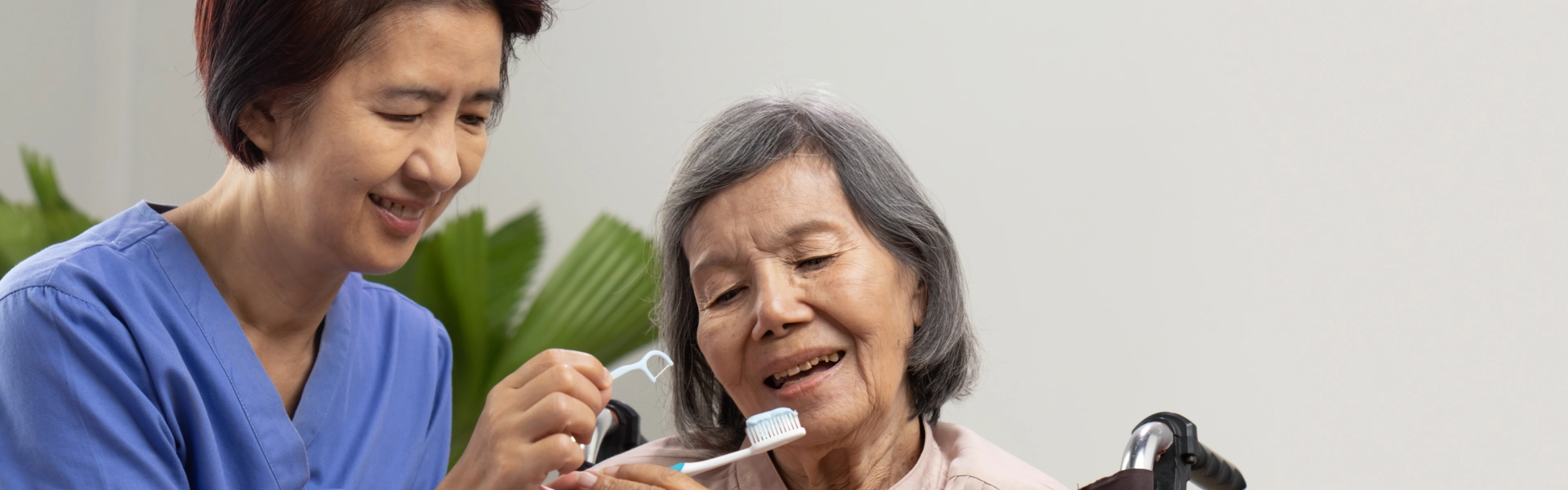 A female caregiver helping an elderly woman to brush her teeth